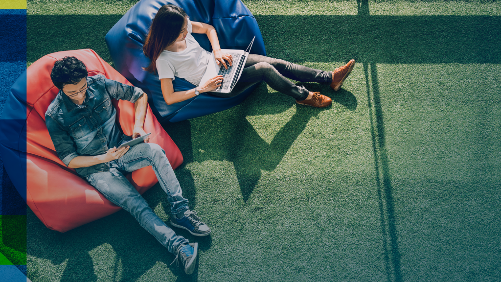 Jovens com jornada de trabalho flexível sentados em pufes no gramado.