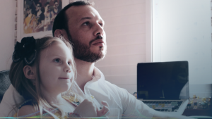 Fernando e sua filha assistindo ao vídeo de canções infantis.