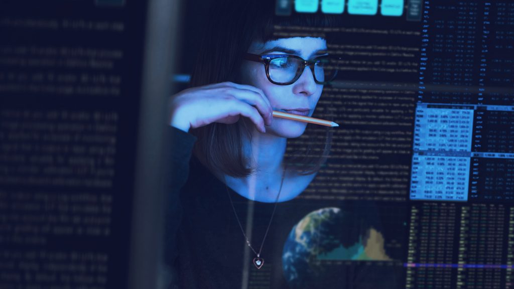 Foto de mulher olhando para tela cheia de números e dados.