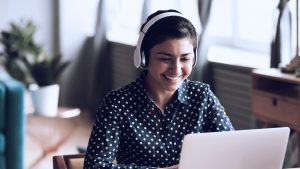 Foto de mulher sorrindo enquanto usa o computador e fones de ouvido.
